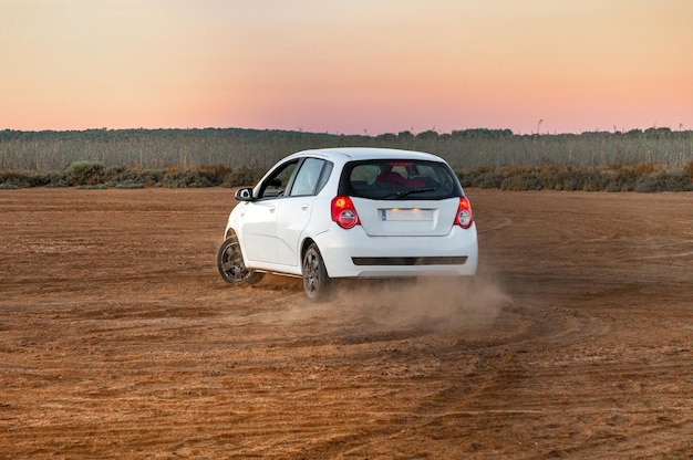 White car drifting on a reddish dirt road at sunrise time