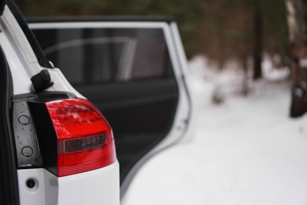 White car with red headlight and open door in winter\
forest