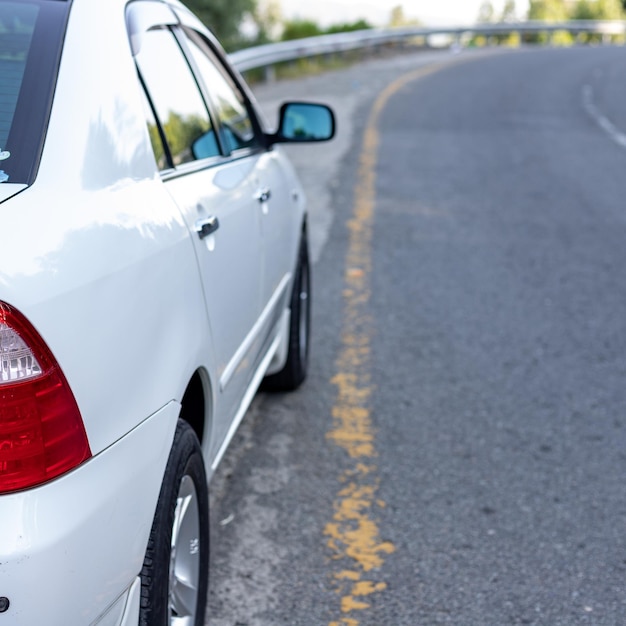 White car with tail lights parked on the side of an asphalt road in the mountain area