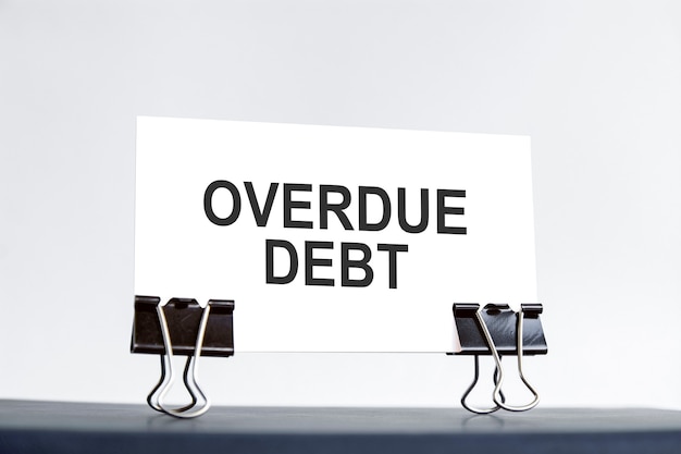 Белая карточка с текстом просроченной задолженности стоит на скрепках на столе на голубом фоне. несосредоточенный.