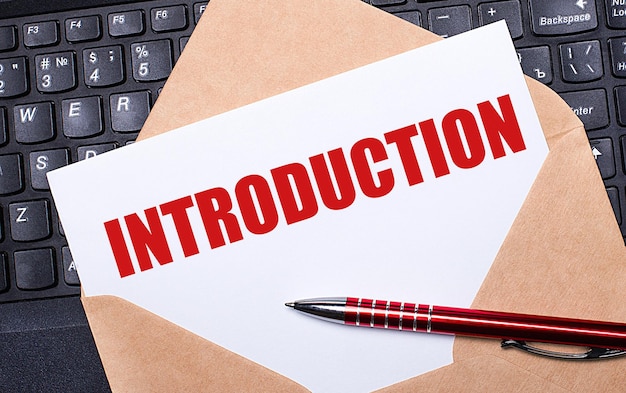 White card with the text INTRODUCTION in a craft envelope on a work desk with a modern laptop keyboard and burgundy pen Flat layout of the workplace