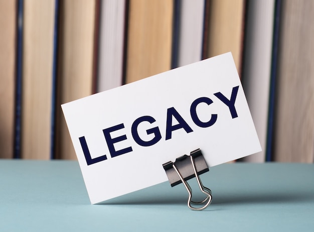 本の背景にテーブルの上の紙のクリップの上に「LEGACY」というテキストが書かれた白いカードが立っています。焦点ぼけ