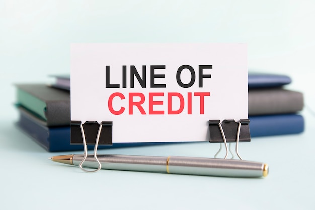 A white card with the text line of credit stands on a clip for papers on the table against the background of books. selective focus