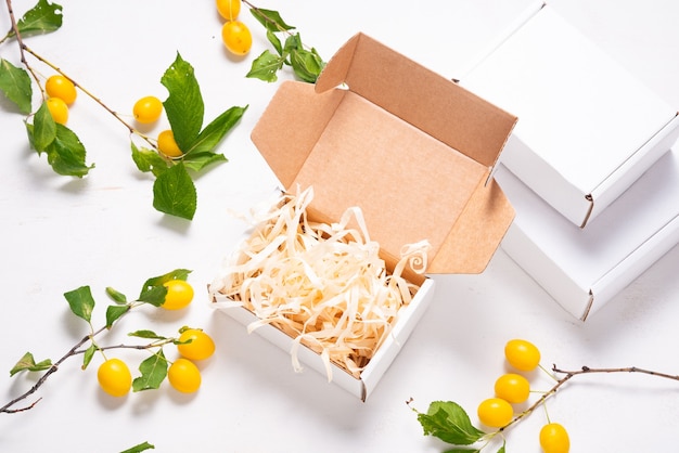 White Cardboard Carton box with paper filler, decorated with fresh plums top view