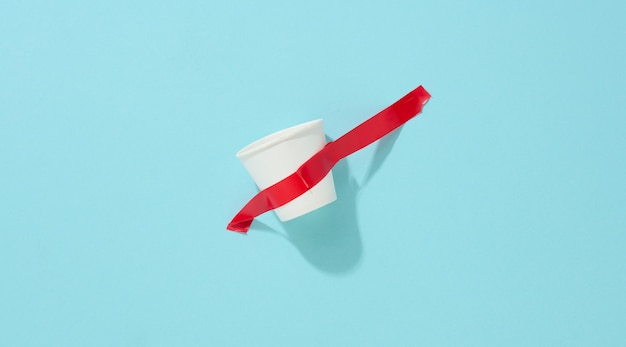 White cardboard cup glued with red sticky tape to the blue background