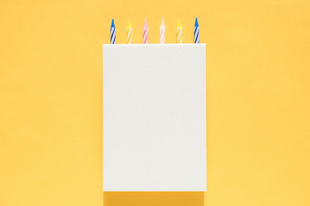 White cardboard vertical poster with cake candles on top on a bright yellow background