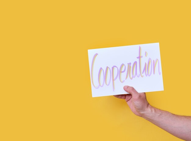 White cardboard with the handwritten text cooperation on yellow isolated background