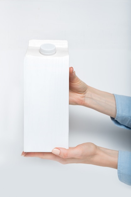 White carton box or packaging of tetra pack with a cap in a female hands. 