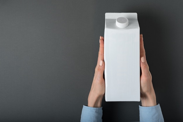 White carton box or packaging of tetra pack with a cap in a female hands. 
