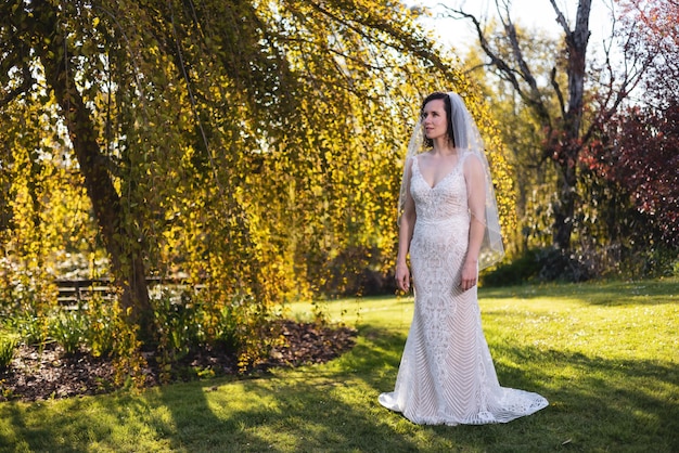 Белая кавказская взрослая женщина в свадебном платье стоит на природе
