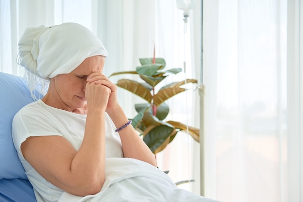 White caucasian female hairless and eyebrowless feel bad are praying and waiting for chemotherapy  in hospital room, breast cancer awareness month concept.