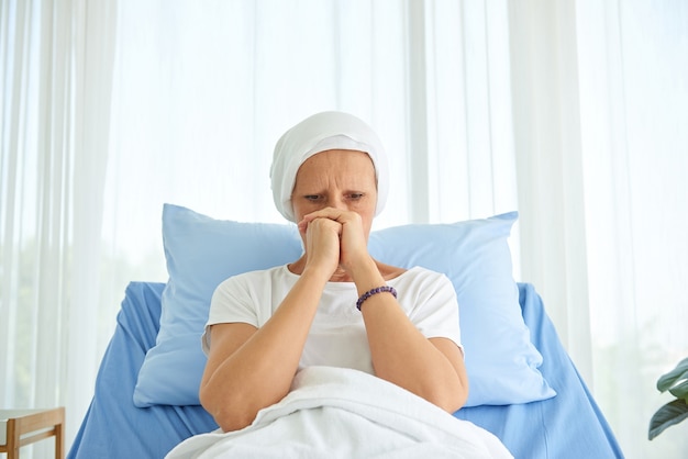 White caucasian female hairless and eyebrowless feel bad are praying and waiting for chemotherapy  in hospital room, breast cancer awareness month concept.