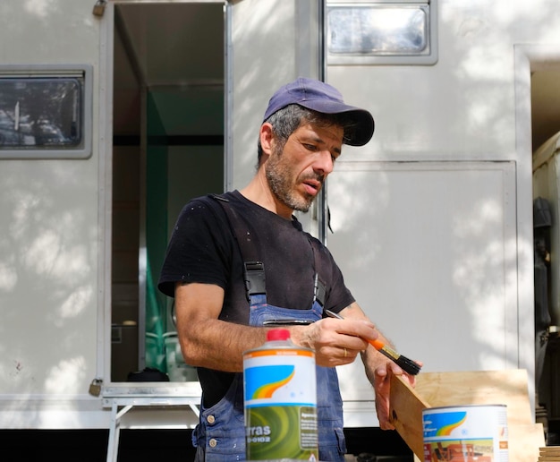 White caucasian man painting wood for the interior of his motor\
home. mobile home repair.