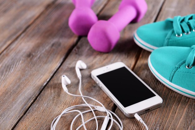 White cellphone with headphones and pink dumb bells and gumshoes on wooden background