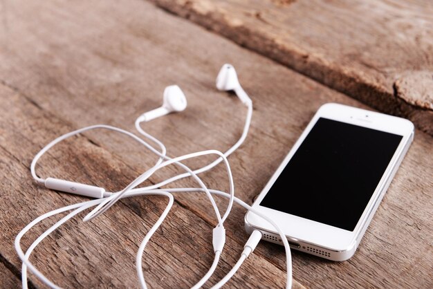 White cellphone with headphones on wooden background