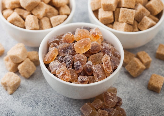 White ceramic bowl plates of natural brown unrefined and caramelized sugar cubes on light background Macro