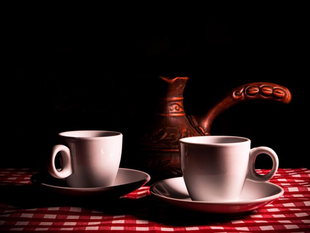 White ceramic coffee cup with saucer and coffee maker on a black background