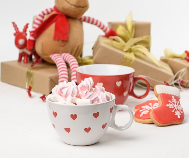 White ceramic cup with cocoa and marshmallows, behind a gift box and a Christmas toy