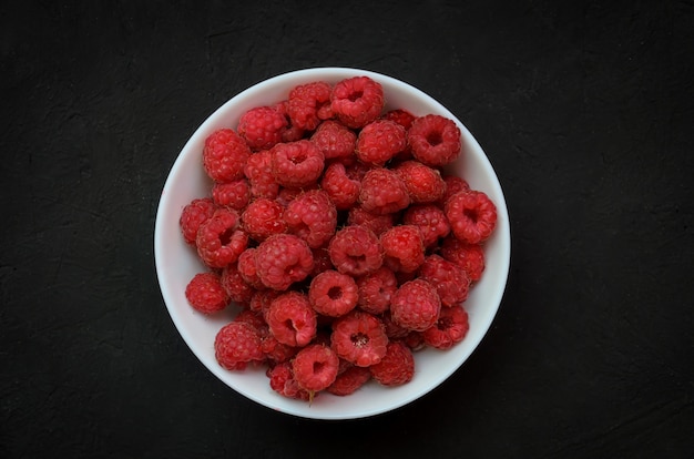 White ceramic plate full of juicy ripe raspberries