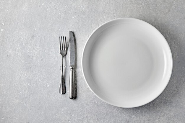 White ceramic plate with cutlery on a light stone table Template for food top view with copy space