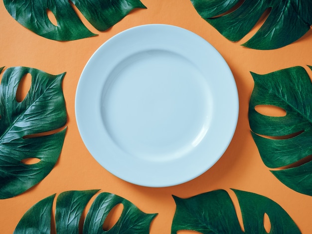 Piatto in ceramica bianca con foglie tropicali monstera su sfondo arancione.