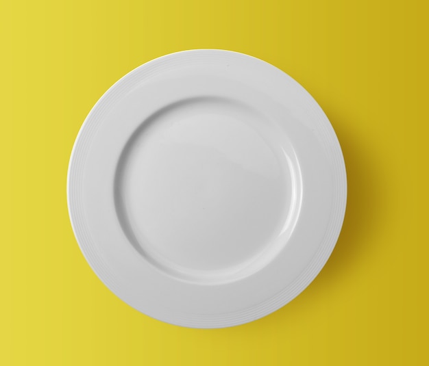 White ceramic plate on yellow background. top view