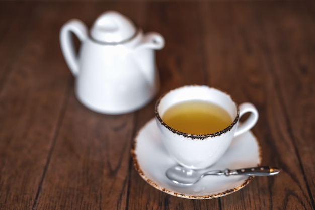 Photo a white ceramic teapot and a cup of tea on a brown wooden table