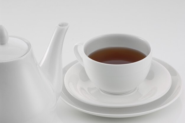 White ceramic teapot with cup on light background, close-up