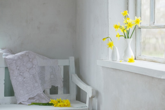 Photo a white chair with a white bench and a vase of daffodils on it.