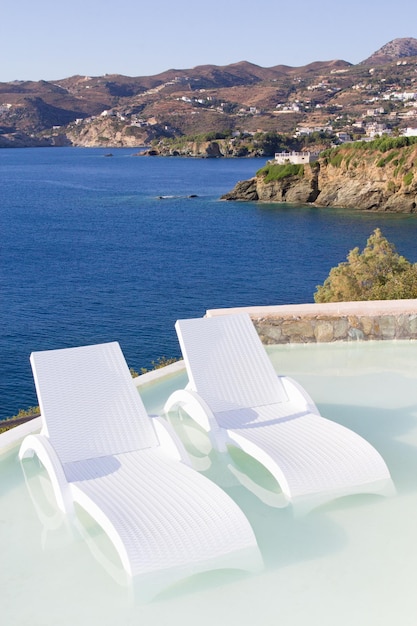 Sedie bianche in piscina con splendida vista mare