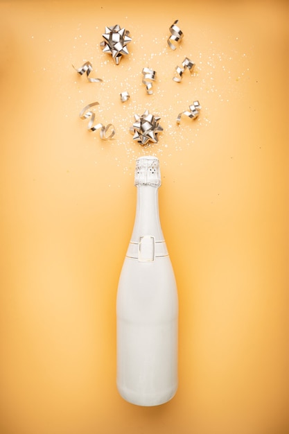 White champagne bottle with glitter and christmas balls on orange gold background flat lay top view