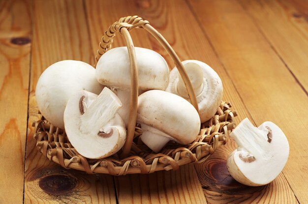 White champignon mushrooms in wicker basket on wooden background