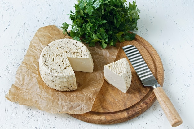 White cheese on a wooden board on a white background with greens