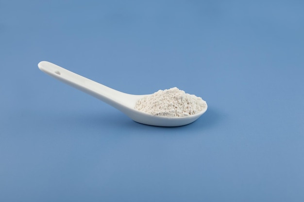 White chemical powder in ceramic spoon on blue Food coloring E171 Titanium dioxide TiO2 Pigment