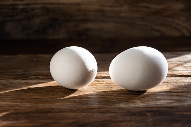 White chicken egg under a sunbeam on a wooden kitchen table.