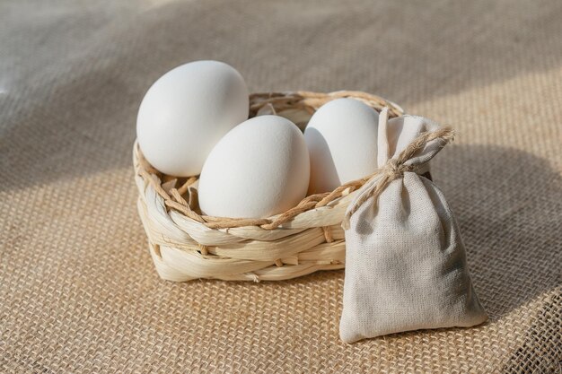 White chicken eggs in a basket on a burlap tablecloth