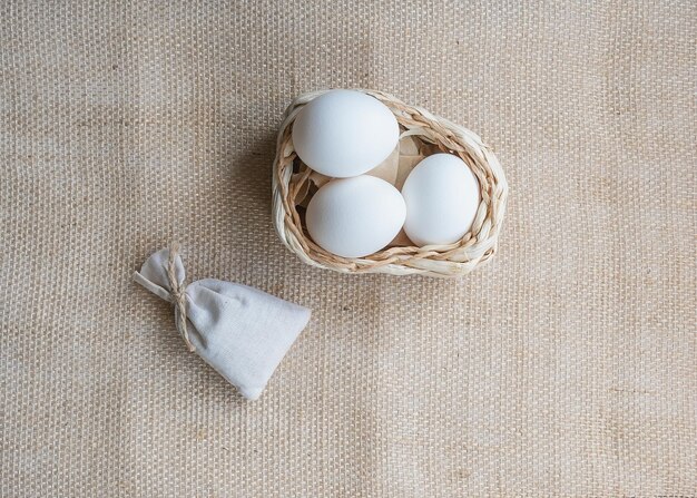 White chicken eggs in a basket on a burlap tablecloth