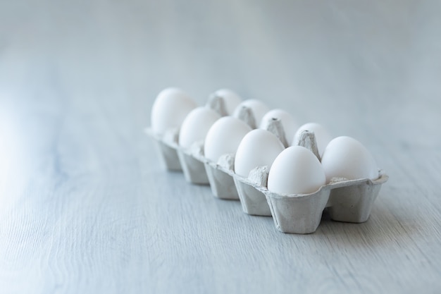 White chicken eggs in an open cardboard box on a light background. A dozen eggs in eco-friendly packaging