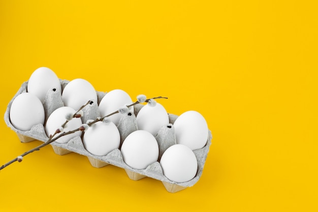 White chicken eggs in an open cardboard box on a yellow background