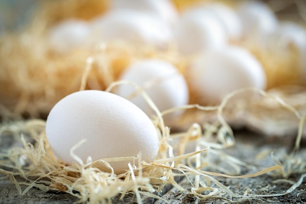 White chicken eggs in the straw nest on a burlap on wooden boards