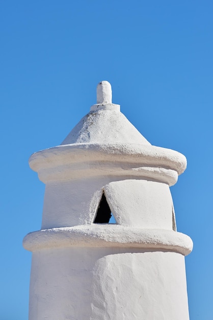 White chimney or bell tower designed on the roof of a house or building against a clear blue sky background with copyspace Construction of exterior architectural structure at a historical monument