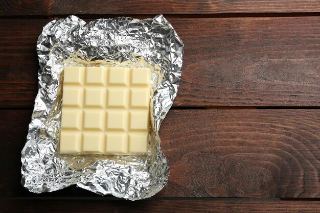 white chocolate bar in foil closeup on wooden background