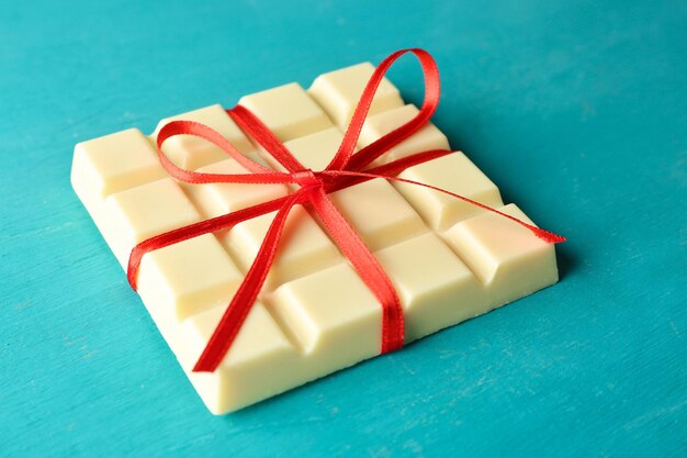 White chocolate bar with red bow on color wooden background