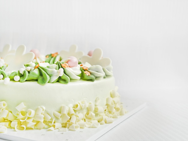 ホワイトチョコレートの誕生日ケーキ。クリーミーで、白と緑で、美しい螺旋状の花びらがあります。白い布の背景に