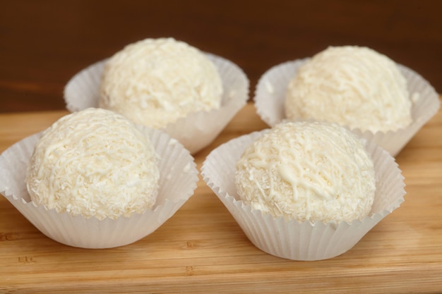 White chocolate candies with coconut topping on wooden surface