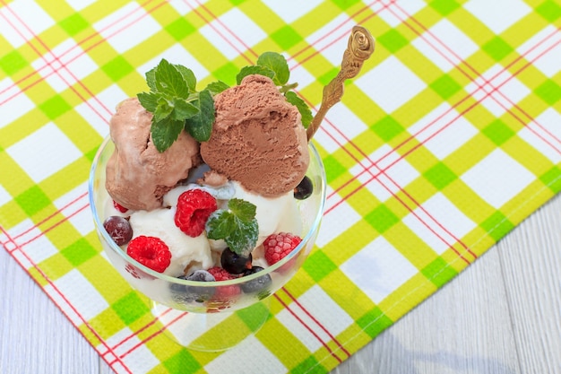 White and chocolate ice cream in a glass with raspberry and currant berries and mint leaves on checkered napkin