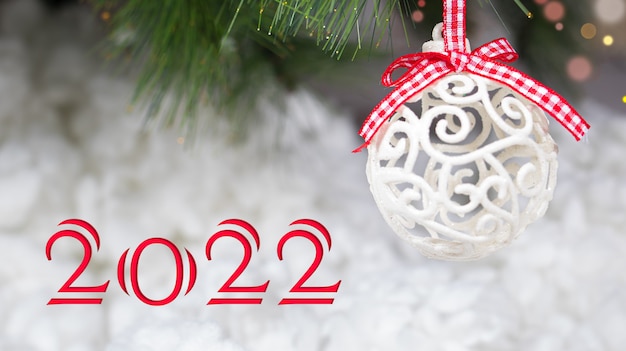 A white Christmas ball and a snow-covered tree branch with the inscription 2022.