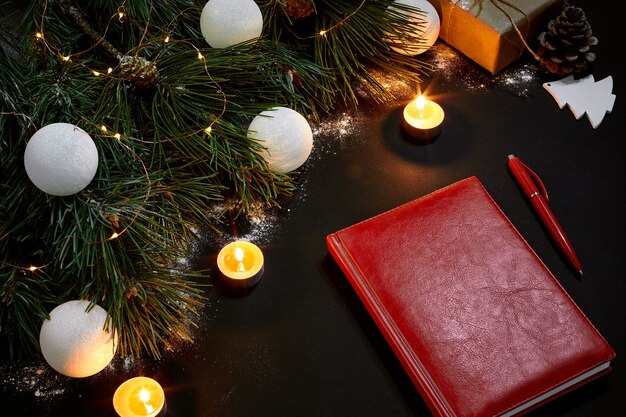 White christmas balls and notebook lying near green spruce branch on black background top view space...