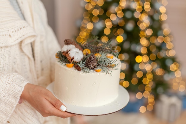 White christmas cake with pines and citrus on bokeh lights\
background. christmas homemade cooking