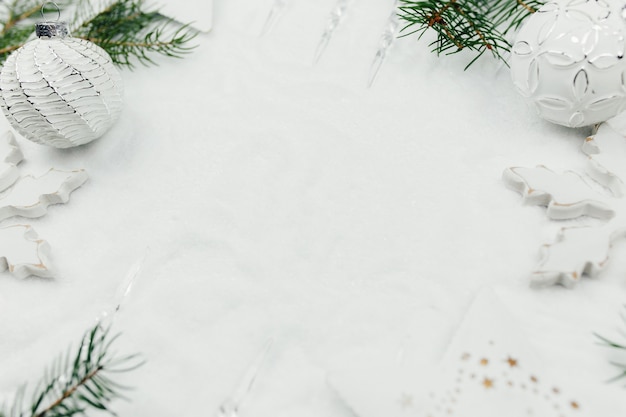 Decorazioni natalizie bianche e rami di abete su neve, sfondo bianco natale, palle di natale bianche.